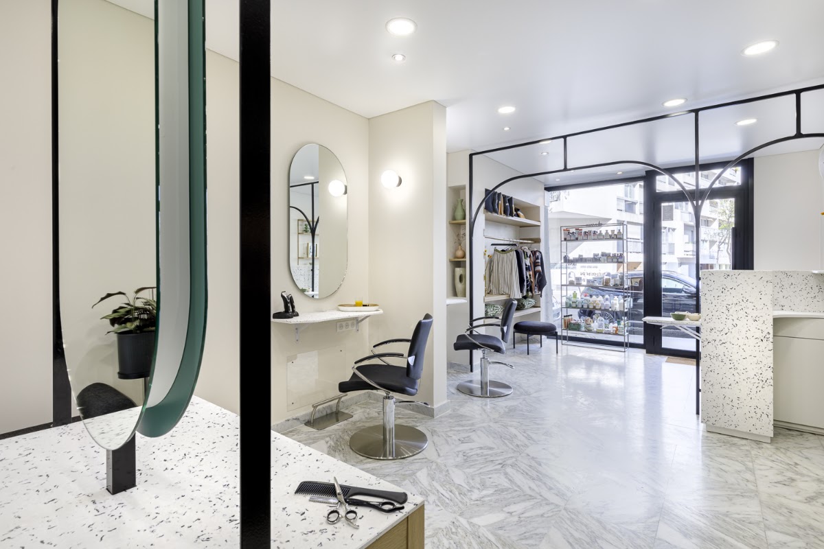 La salle du salon : sol de marbre, plans en terrazzo, arches d'acier noir portant les miroirs ovales, et la vitrine sur l'avenue.